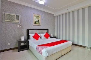 Habitación de hotel con una cama grande, una mesita de noche, aire acondicionado montado en la pared y un muro a rayas.