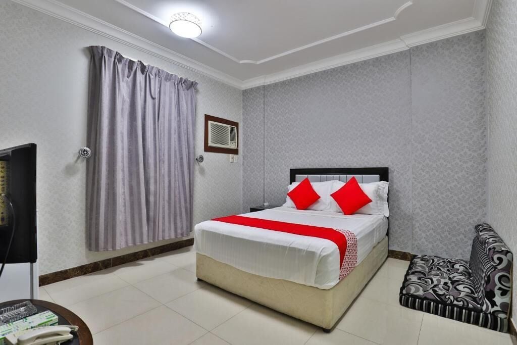 A hotel room with a bed, a television, a bedside table, a patterned sofa, and a curtain.