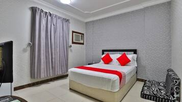 A hotel room with a bed, a television, a bedside table, a patterned sofa, and a curtain.
