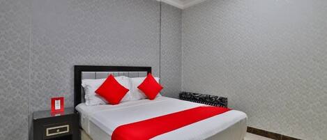 A hotel room with a bed, a nightstand, and a red throw blanket.