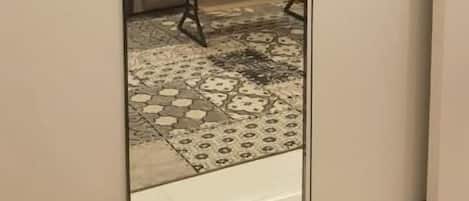 A room with a large mirror reflecting a sofa, a small table, and a patterned rug.
