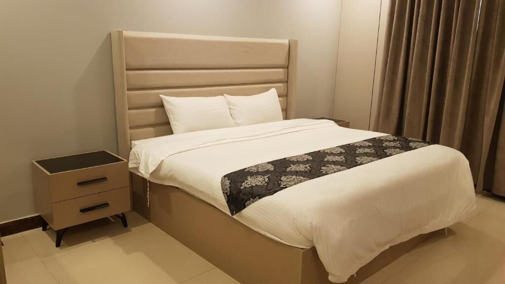 A bed with a headboard, a bedside table with drawers, and a patterned throw on the bed.