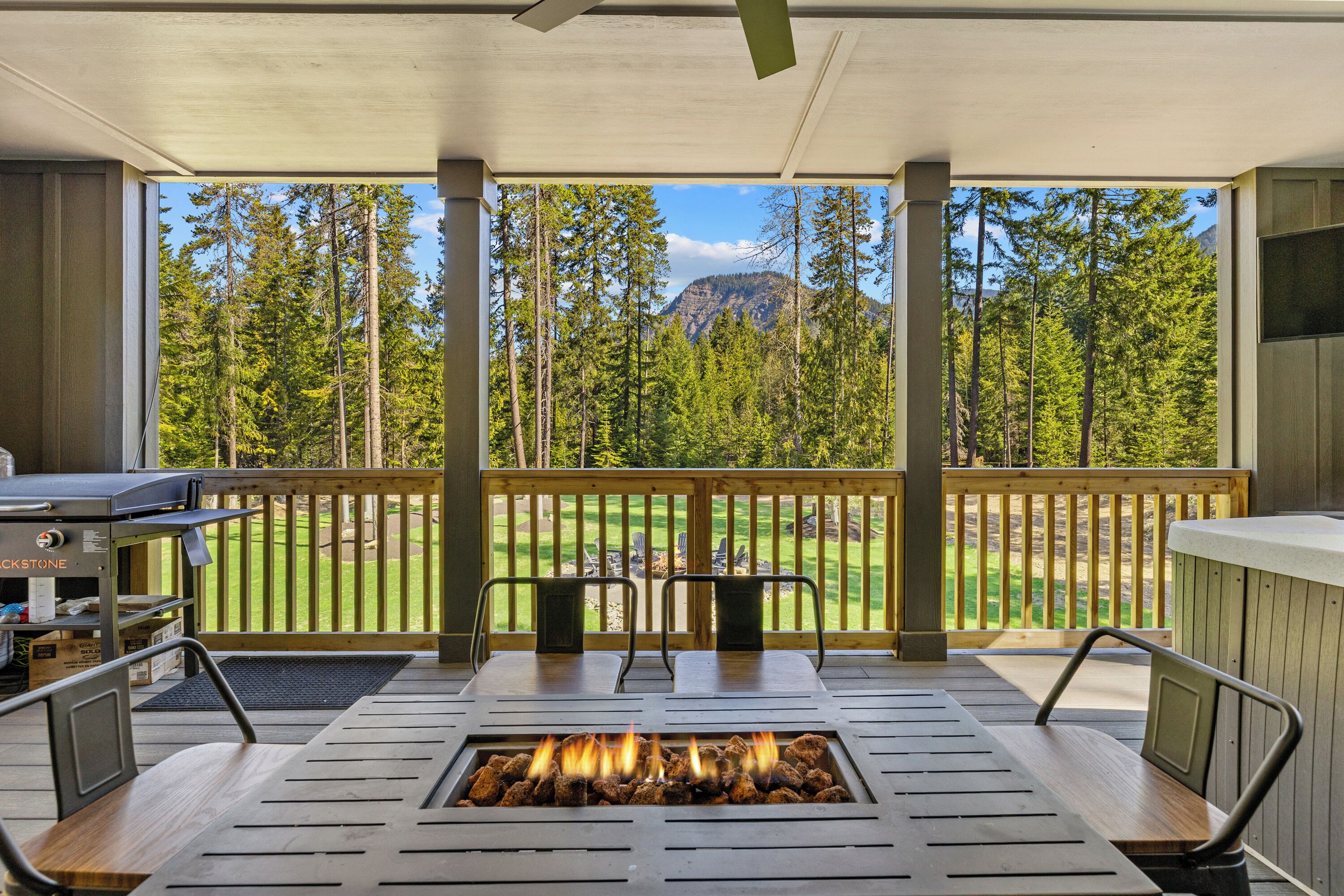 A covered outdoor area with a fire pit, seating, and a view of a forest and mountains.