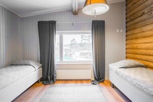 Una habitación con dos camas, una ventana con cortinas, un radiador y una pared de madera.