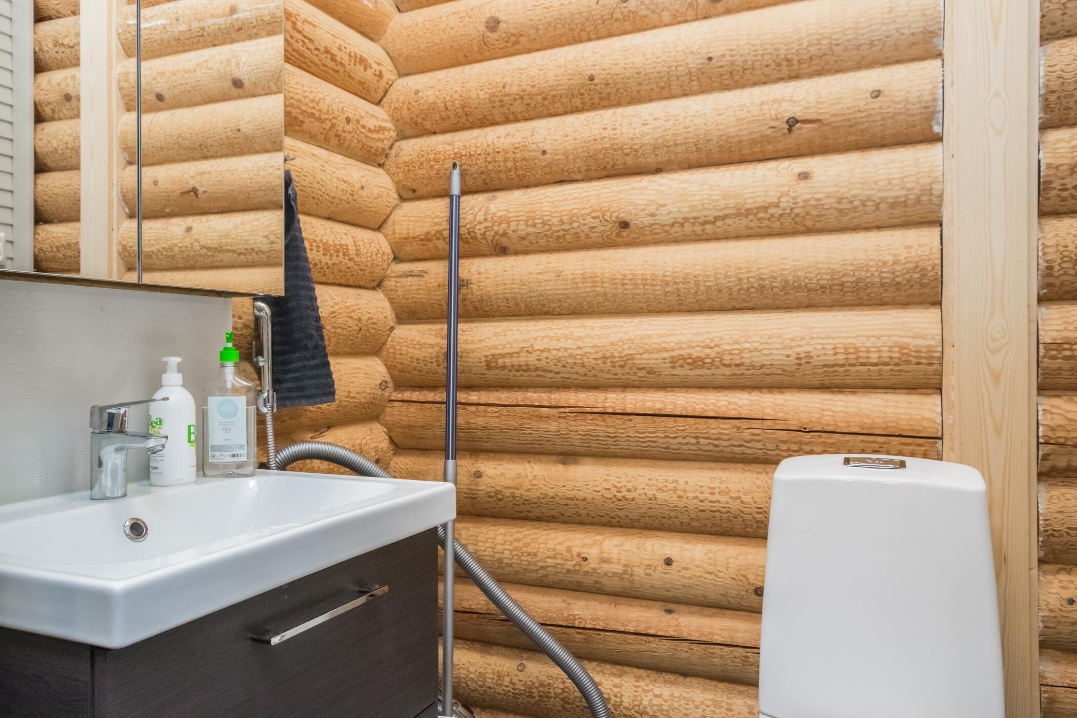 A bathroom with a wooden log wall, a sink with a mirror, and a white toilet.