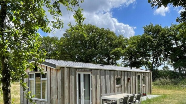 Una pequeña cabaña de madera con un patio, una mesa y sillas.