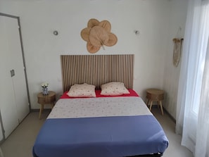 Un dormitorio con un cabecero a rayas, una decoración floral grande en la pared, dos mesitas de noche y una cama con colcha azul y blanca.