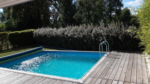 A rectangular swimming pool with a wooden deck surrounding it. - Maison avec piscine sur un golf (Fiac)