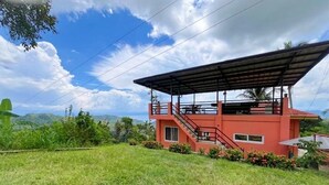 Un edificio de dos pisos con fachada roja, un área exterior techada y una escalera que conduce al nivel superior.