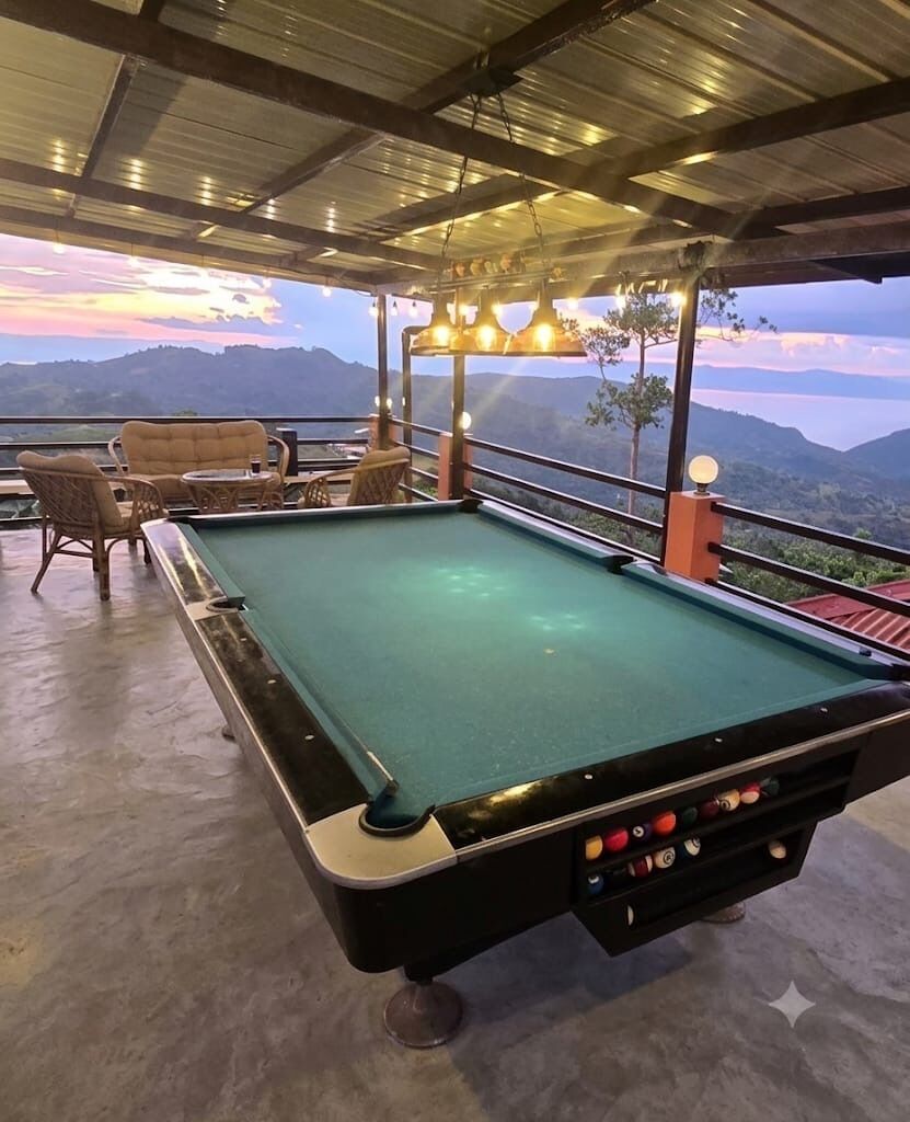 A pool table with surrounding chairs and tables, set against a scenic mountain backdrop.