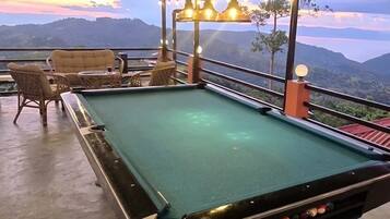 A pool table with surrounding chairs and tables, set against a scenic mountain backdrop.