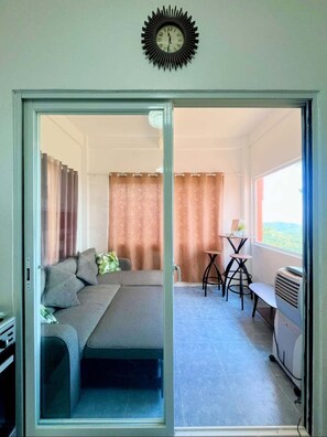A room with a sofa, a table with chairs, a heater, and a view through a glass door.