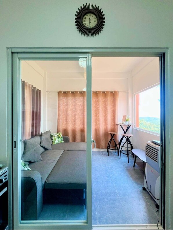 A room with a sofa, a table with chairs, a heater, and a view through a glass door. - Salamanca Mountain Retreat w/ Stunning Sunset Views, Billiards, Karaoke &Firepit (Oslob)