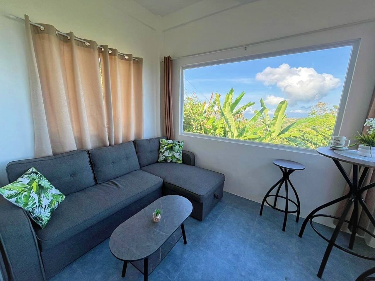 A modern living room with a grey sectional sofa, a small round table, and a window with a view of greenery.