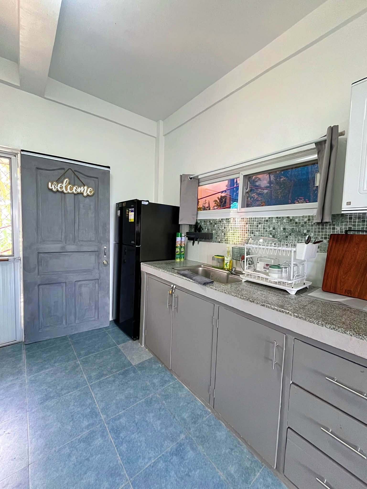 Une cuisine équipée d’un réfrigérateur, de placards, d’un évier et d’une pancarte de bienvenue sur la porte.