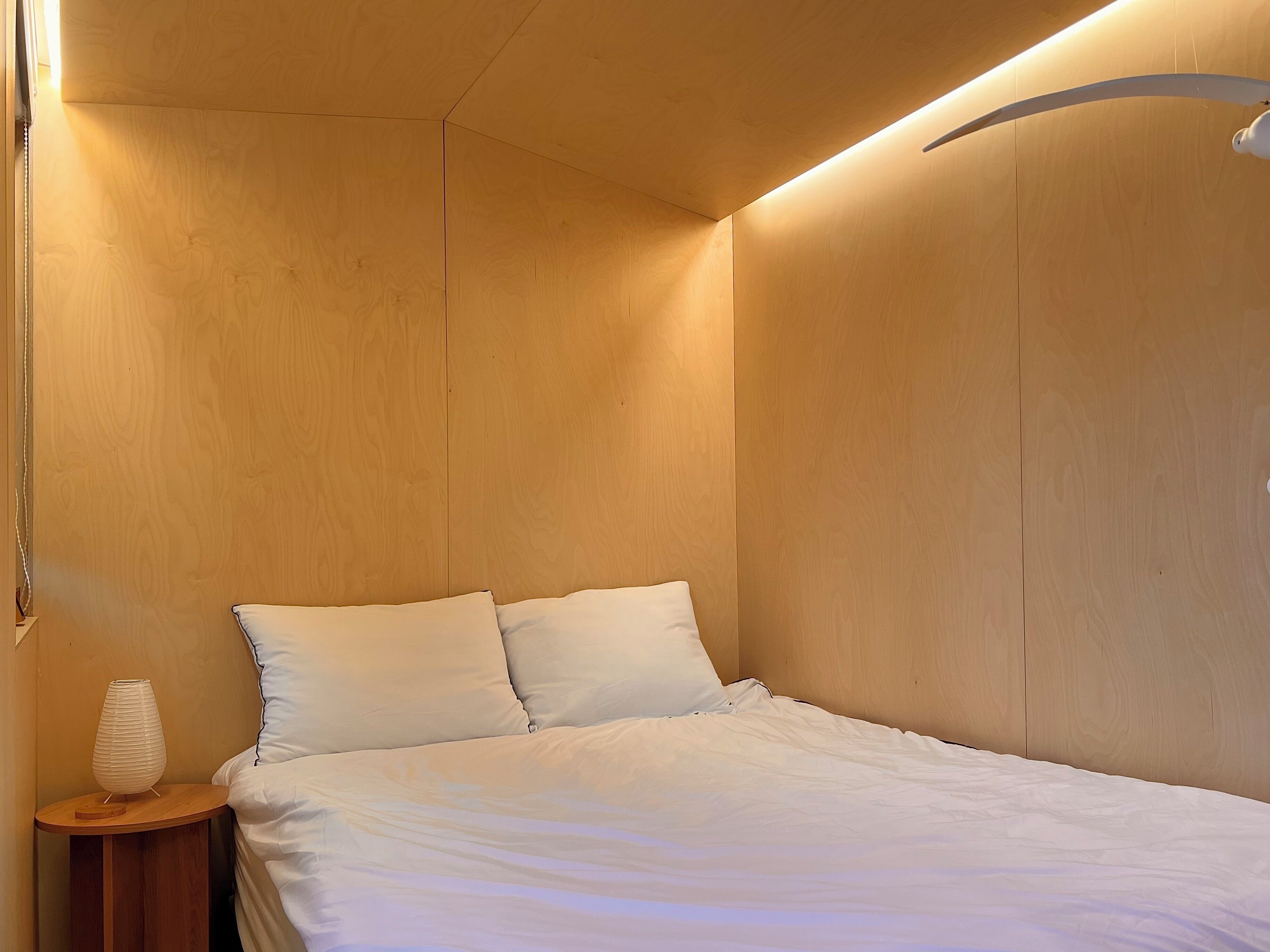 Un dormitorio con una cama, dos almohadas, una mesita de noche con lámpara y paredes de madera.