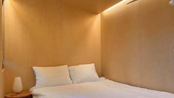 Un dormitorio con una cama, dos almohadas, una mesita de noche con lámpara y paredes de madera.