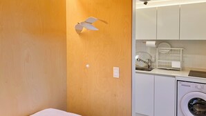Una stanza compatta con parete in legno, una ventola a soffitto, una lavatrice e un angolo cottura con lavello e scolapiatti.