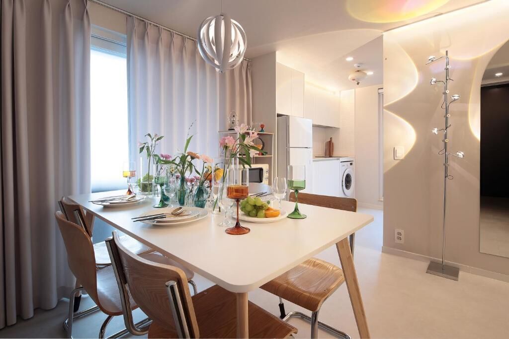 Un comedor moderno con una mesa blanca, sillas marrones y un jarrón con flores.