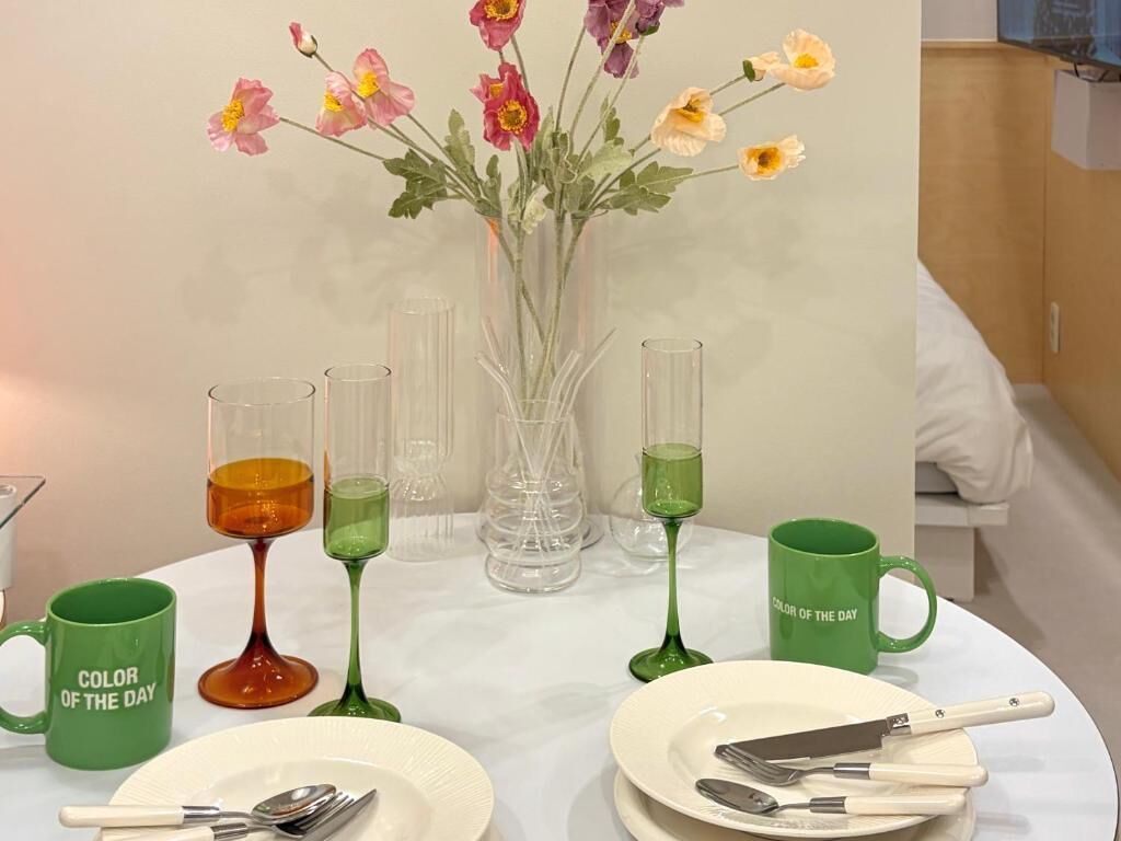 Une table dressée avec un vase de fleurs, une tasse verte et une assiette blanche avec des couverts.
