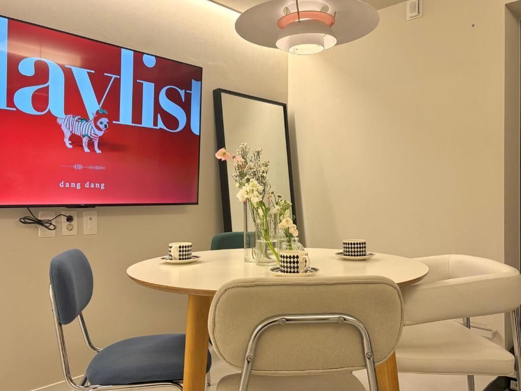 A conference room with a round table, two chairs, a large TV screen, and a vase with flowers.