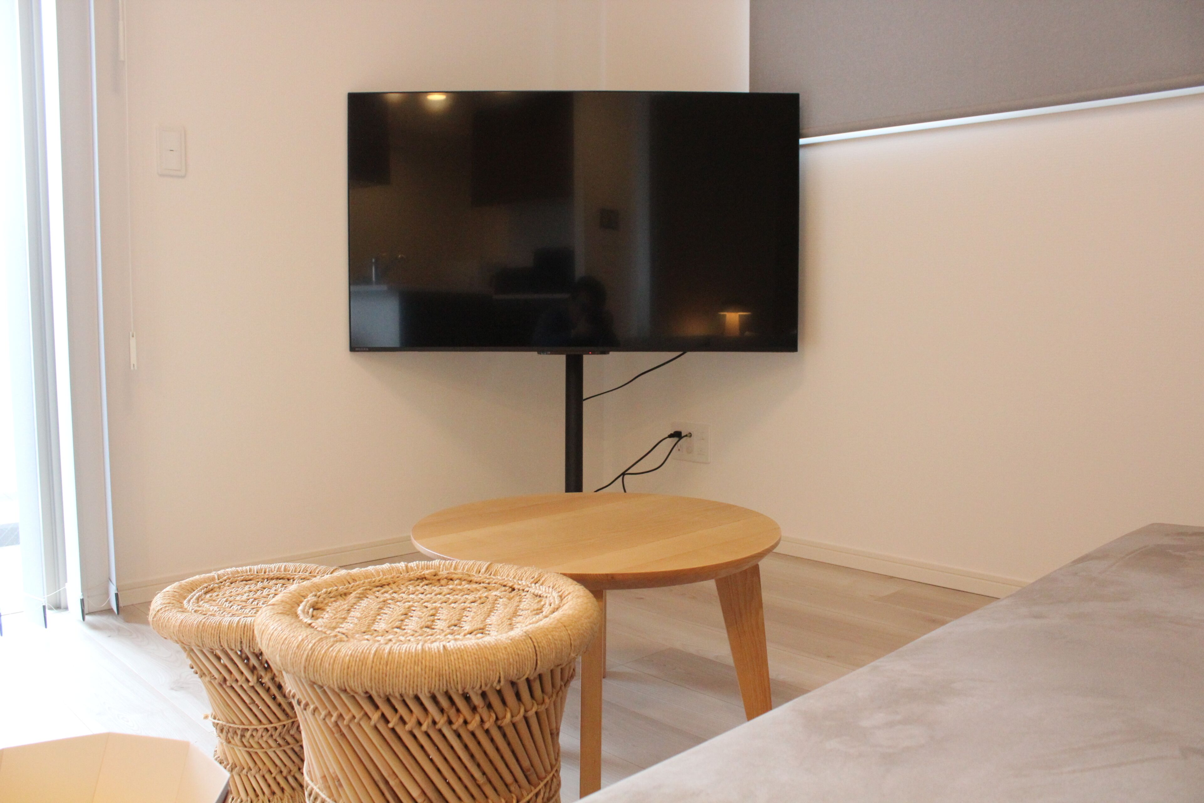 Una sala de estar moderna con un televisor de pantalla plana montado en la pared, una mesa redonda de madera y dos sillas tejidas.