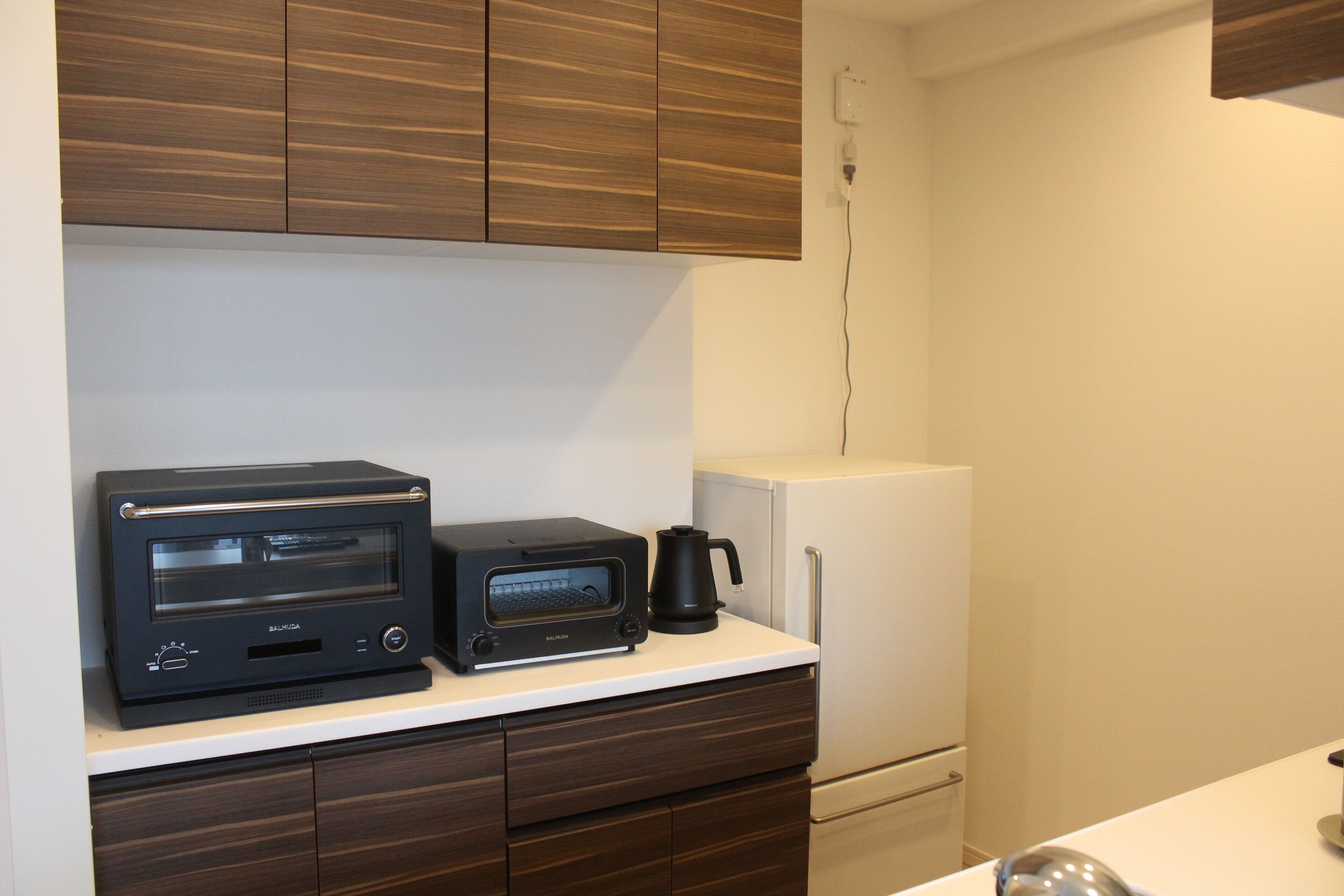 Una kitchenette con un horno tostador negro, una cafetera negra y un refrigerador blanco.