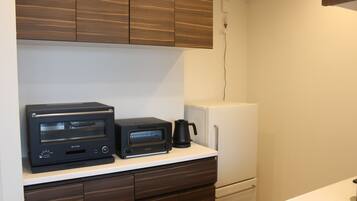 Una kitchenette con un horno tostador negro, una cafetera negra y un refrigerador blanco.