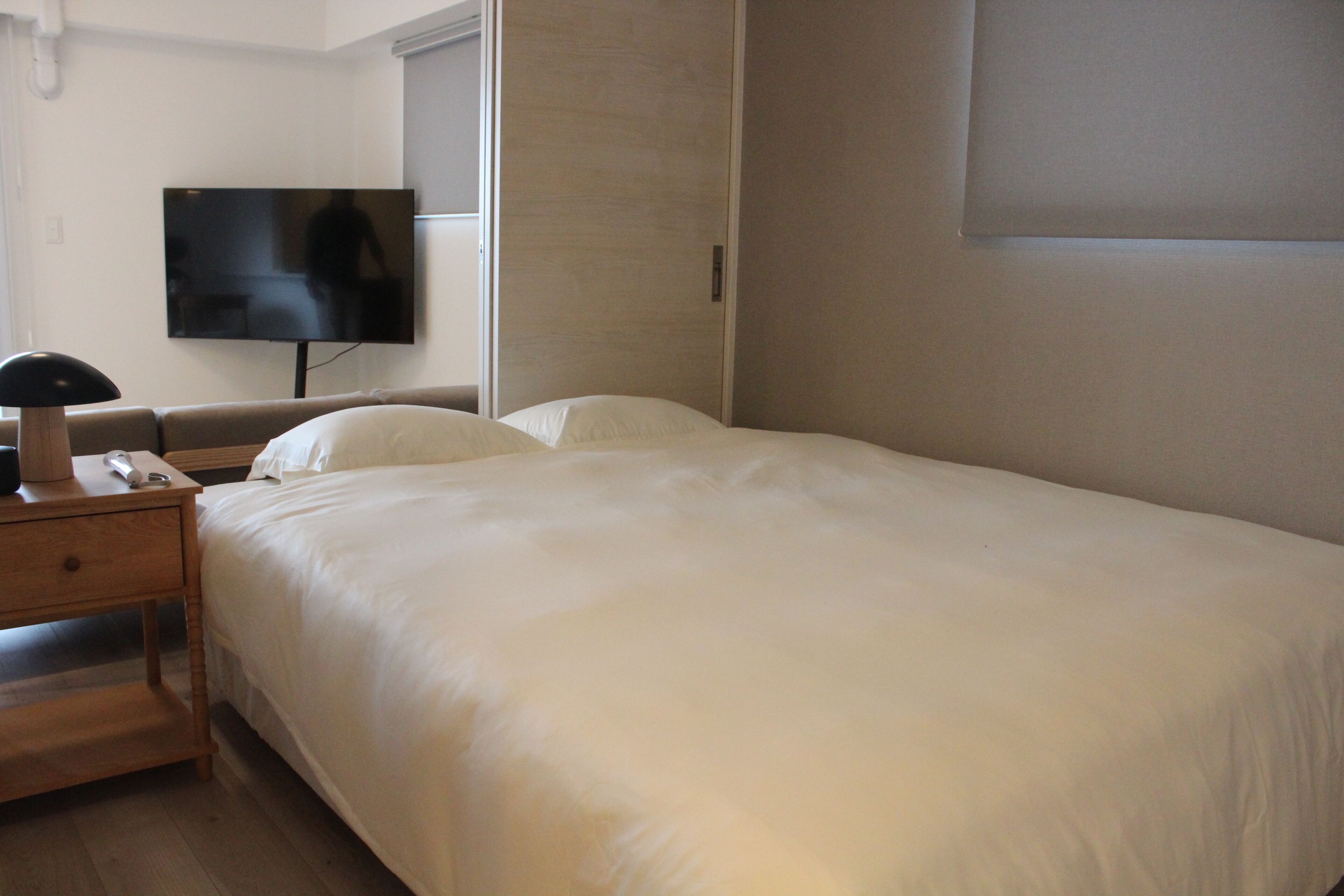 Habitación de hotel con cama, mesita de noche con lámpara, televisor y ventana con persianas.