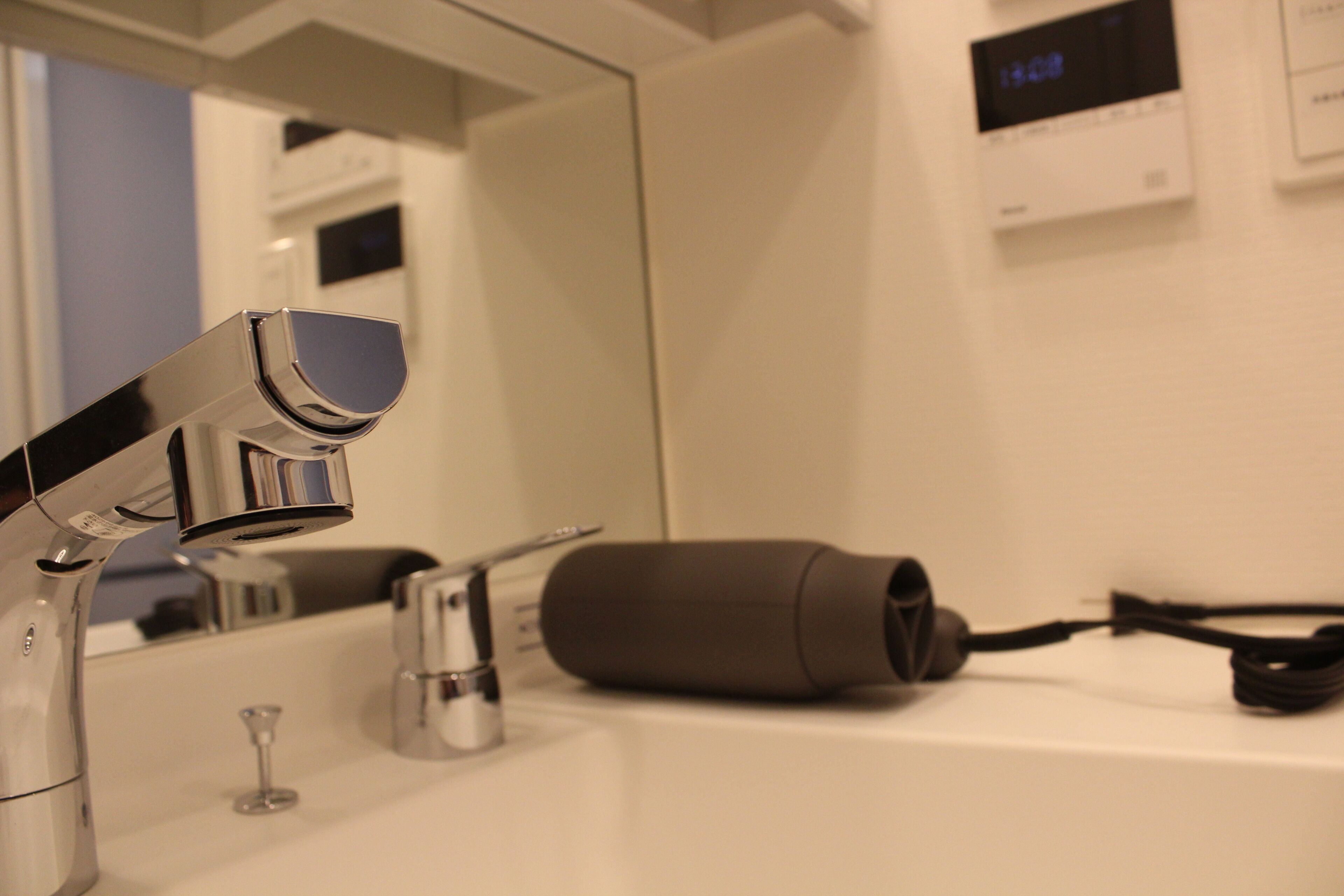 A bathroom with a modern sink, a hairdryer, and a digital clock on the wall.
