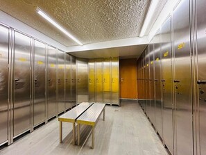 A row of metallic lockers with numbers on them, a bench in the center, and a textured ceiling. - Hotel Alpin Superior (Saas-Fee)