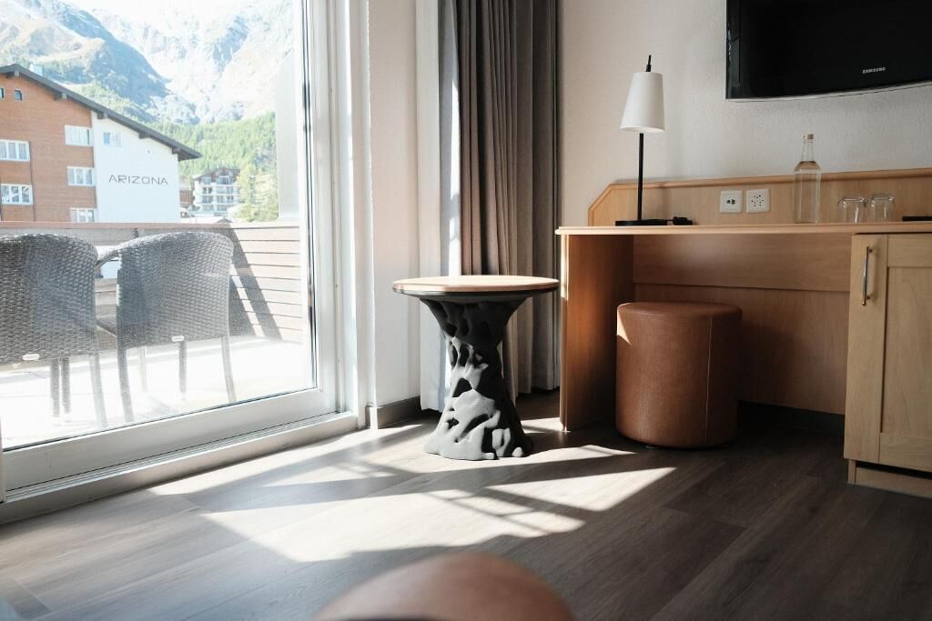 A hotel room with a large window, a wooden desk, a television, and a view of a building labeled 'ARIZONA.'