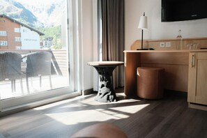 A hotel room with a large window, a wooden desk, a television, and a view of a building labeled 'ARIZONA.' - Hotel Alpin Superior (Saas-Fee)