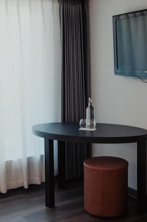 A room with a round table, a stool, a bottle, and a TV mounted on the wall. - Hotel Alpin Superior (Saas-Fee)