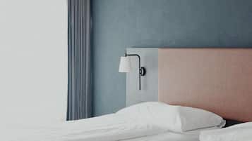 Una camera d'albergo con un letto, una lampada a parete e una finestra con tende.