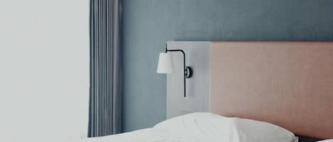 A hotel room with a bed, a wall-mounted lamp, and a window with curtains.