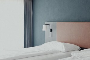 A hotel room with a bed, a wall-mounted lamp, and a window with curtains. - Hotel Alpin Superior (Saas-Fee)