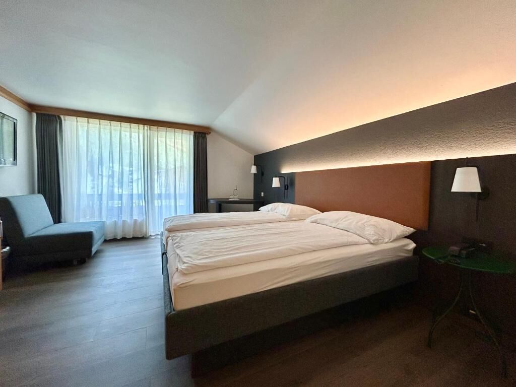 Une chambre d’hôtel équipée d’un lit, d’un bureau, d’une chaise et offrant une vue sur la ville grâce à de grandes fenêtres.