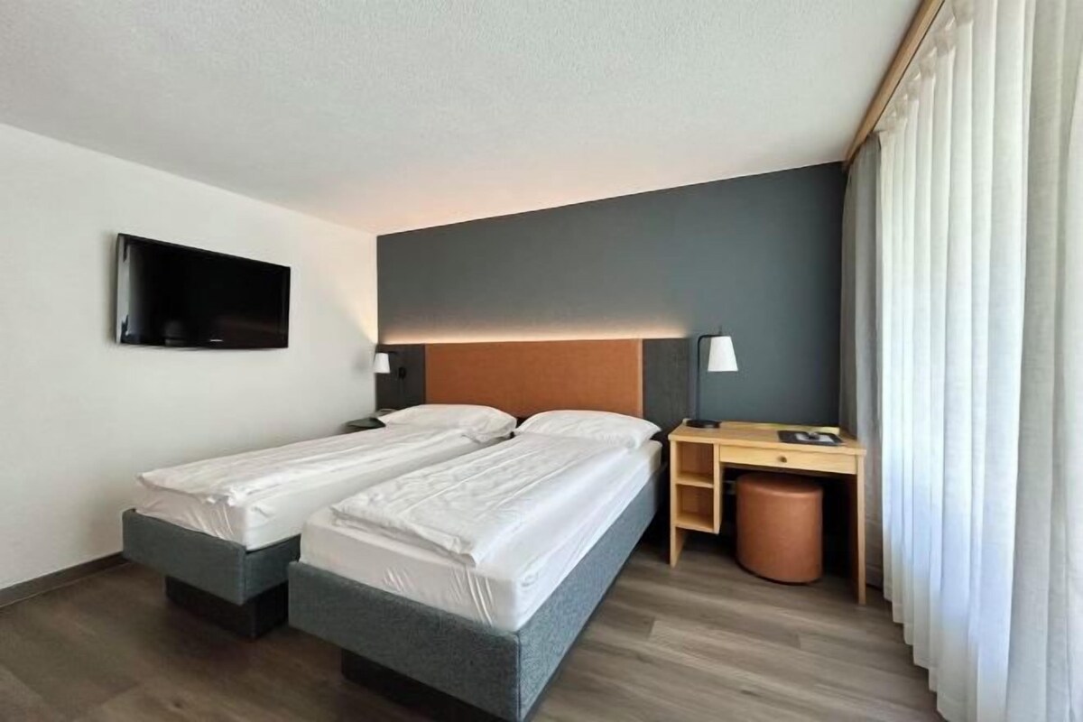 Habitación de hotel con dos camas, un escritorio, un televisor y un cesto de basura.