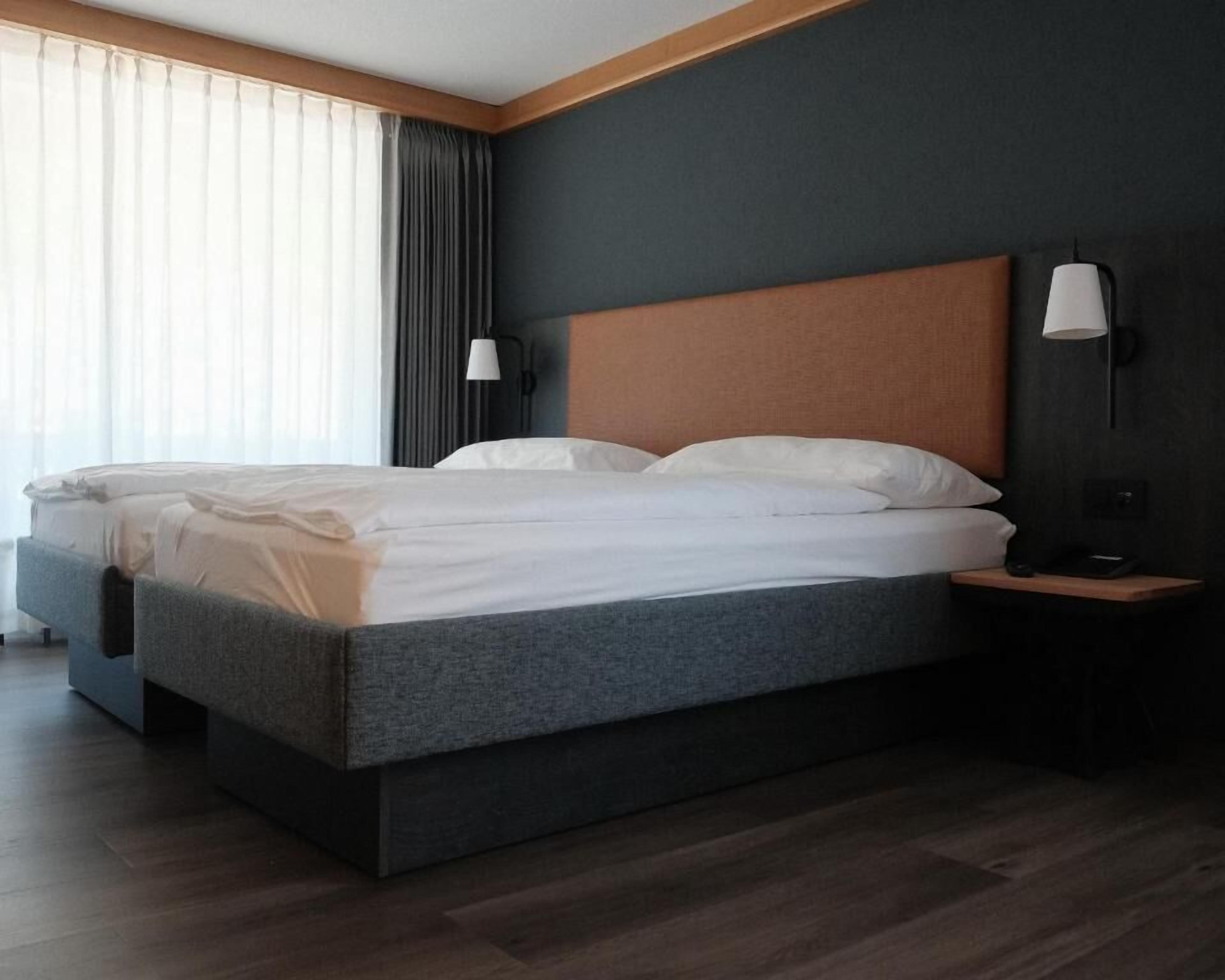 A modern hotel room with a large bed, a wooden headboard, and a nightstand with a lamp.