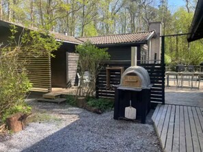 Un espacio exterior rústico con una terraza de madera, un horno de piedra y una valla de madera.