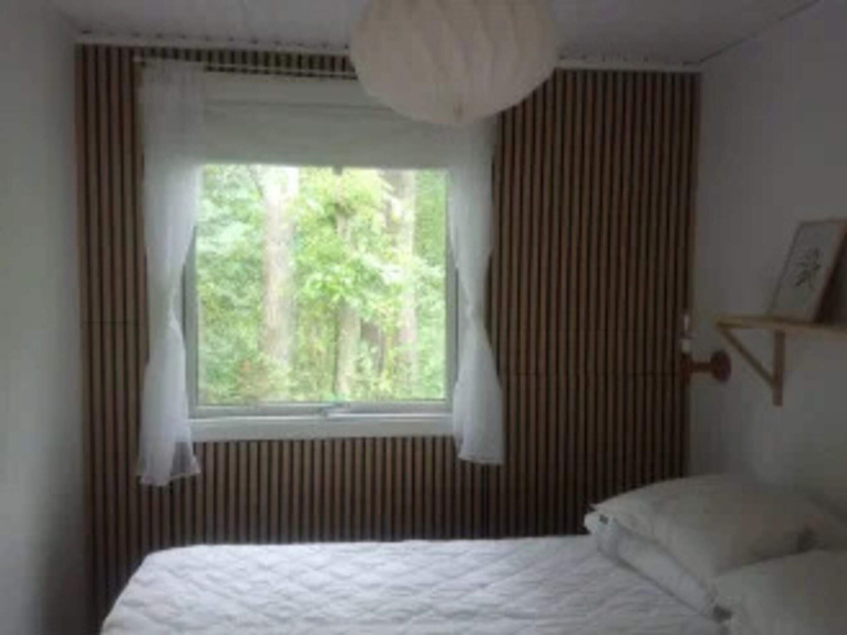 A bedroom with a bed, a window with curtains, and a wall-mounted shelf with a picture.