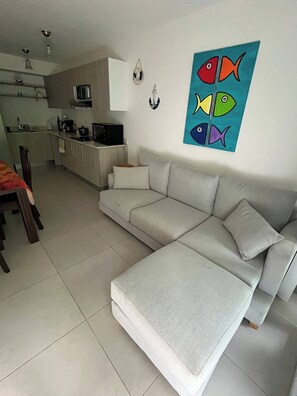 A modern living room with a grey sectional sofa, a dining area with a table and chairs, and a kitchen in the background. - Great Apartment Costa Rica, Punta Esmeralda (Tárcoles)