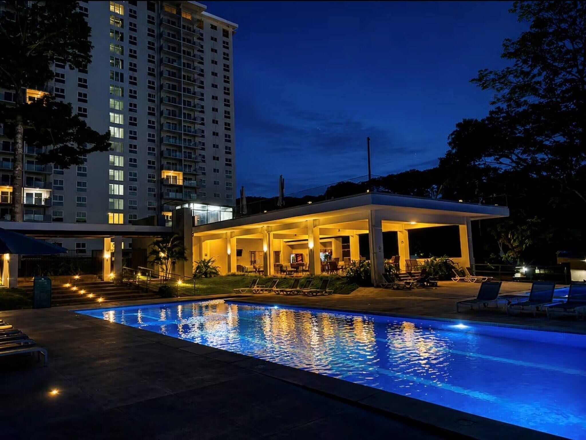 A swimming pool with lounge chairs and a covered seating area at dusk.