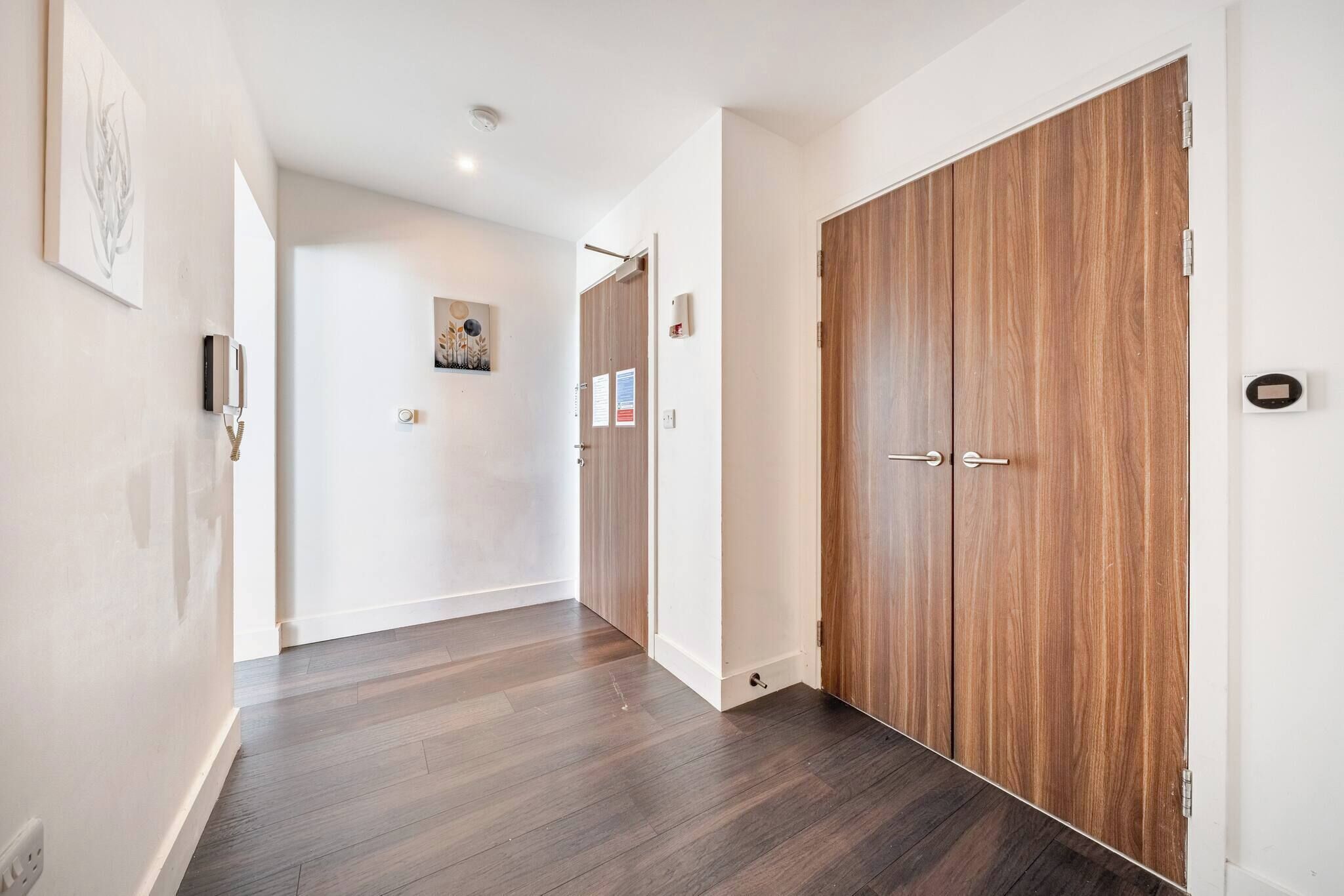 A hallway with wooden flooring, a double door, and a wall-mounted intercom.