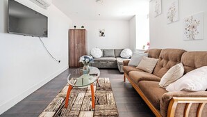 Uma sala de estar moderna com um sofá, uma mesa de centro de vidro e uma TV fixada na parede.