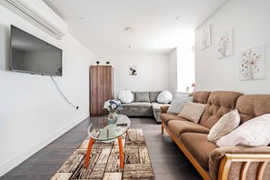 Ein modernes Wohnzimmer mit einer Couch, einem Glastisch und einem an der Wand montierten Fernseher.
