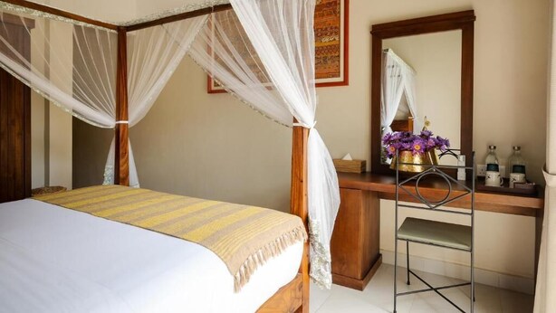 A bedroom with a four-poster bed, a wooden desk, a chair, and a bedside table with a vase of flowers. - Rekawa Wellness Resort  (Netolpitiya)