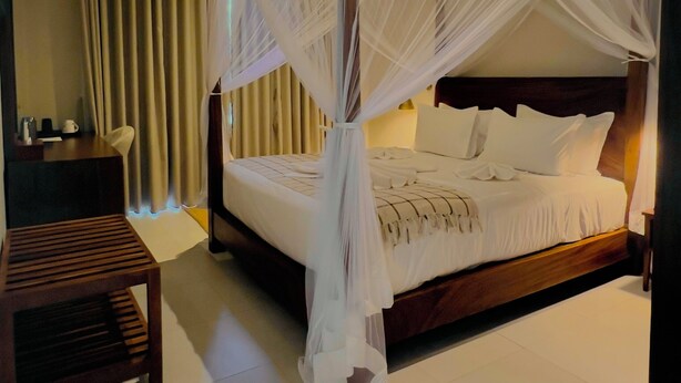 A bedroom with a canopy bed, a bedside table, a chair, and a wooden bench. - Rekawa Wellness Resort  (Netolpitiya)