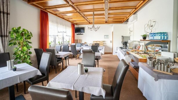 Comedor de hotel con mesas, sillas, un bufé y una planta grande.